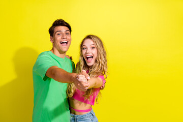 Portrait of two nice young partners hold hands dance empty space wear t-shirt isolated on vibrant yellow color background