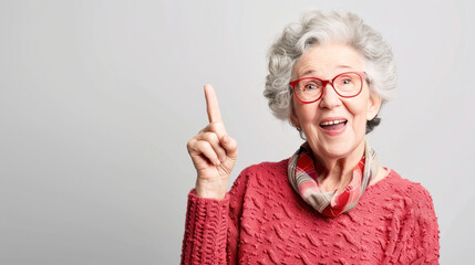 Joyful senior woman with gray hair and red glasses pointing upwards