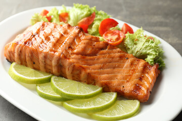 Delicious grilled salmon fillet with vegetable salad and lime on grey table, closeup