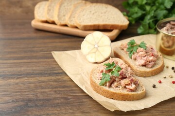 Sandwiches with canned meat, parsley, garlic and peppercorns on wooden table, closeup. Space for text