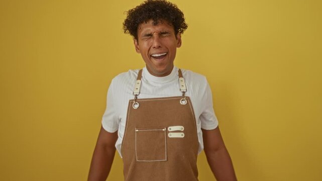 Handsome young hispanic man wearing apron over isolated yellow background yawning and stretching arms