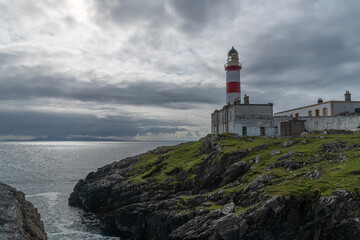 Looking out across the Minch to the Isle of Skye, the red and white Eilean Glas Lighthouse on the east coast of the island of Scalpay in the Outer Hebrides, Scotland, UK
