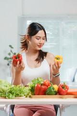 Young woman is smiling while choosing a bell pepper for her salad, surrounded by fresh vegetables on a table