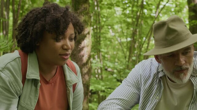 Handheld shot of two mature friends examining bushes with berries while walking in forest