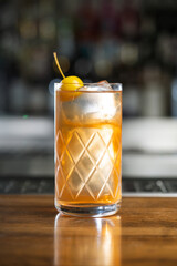 Highball glass with alcoholic cocktail decorated with a yellow cocktail apple served on counter of bar on blurred background with bokeh. Vertical photo