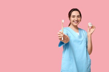 Young female dentist with dental floss and toothbrush on pink background