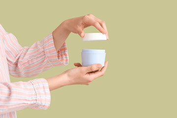 Woman holding opened jar of cream on green background