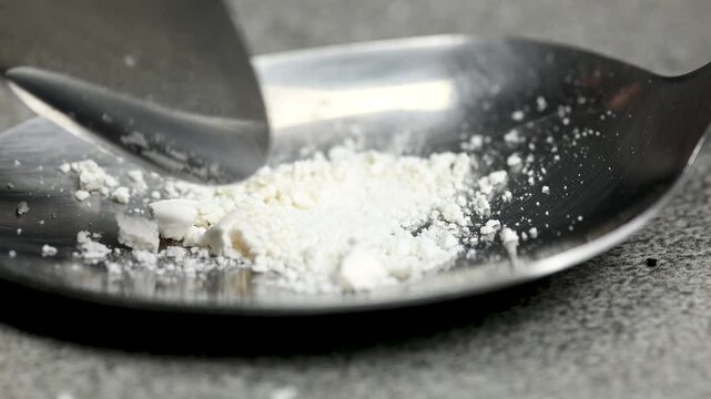 White pill being crushed under a spoon on black background, health care medicine concept, macro, close up