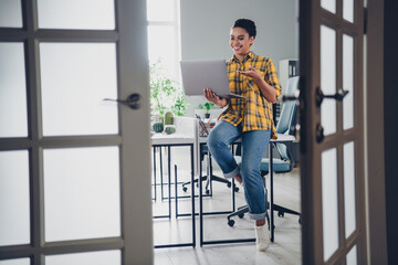 Full length photo of lovely young lady sit table laptop video call dressed yellow plaid shirt...