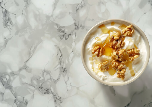Bowl of creamy yogurt topped with crunchy walnuts and drizzled with honey, served on a white marble surface, ideal for a healthy and nutritious snack