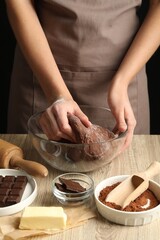 Woman kneading chocolate dough at wooden table, closeup