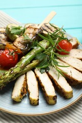 Delicious grilled vegetables and cut chicken meat on light blue table, closeup