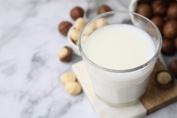 Glass of macadamia milk and nuts on white marble table, closeup. Space for text