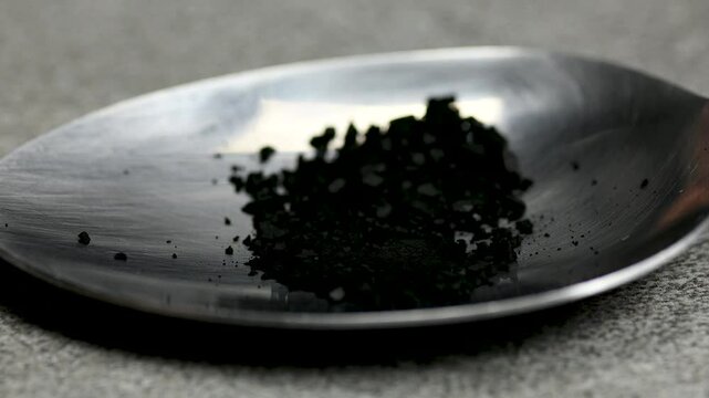Black pill being crushed under a spoon on black background, health care medicine concept, macro, close up