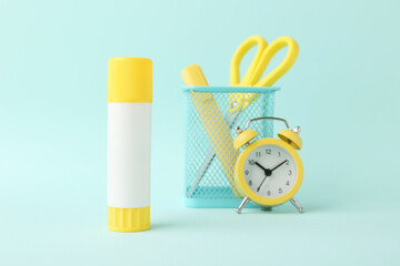 Glue stick, alarm clock, holder and scissors on turquoise background