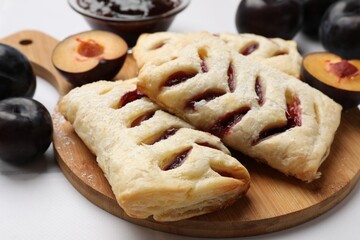 Delicious puff pastries and plums on white table, closeup