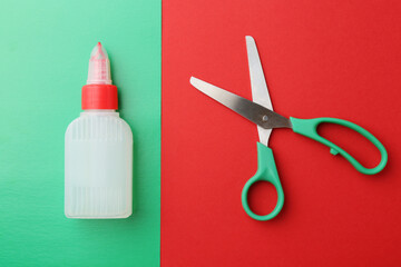 Bottle of glue, scissors and green paper on red background, flat lay