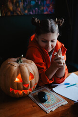Caucasian happy girl orange color cloths near carved Halloween pumpkin studying online laptop