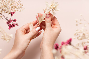 Spring manicure of women's hands with white gel polish and dried flower design. Female hands hold...
