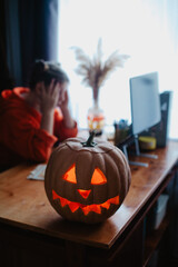 Caucasian happy girl orange color cloths near carved Halloween pumpkin studying online laptop