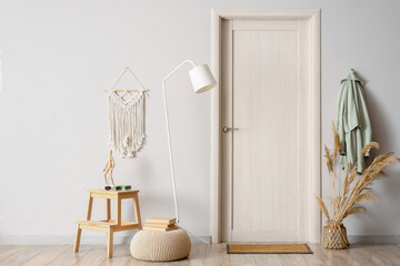 Modern interior of hallway with pouf, floor lamp, step ladder and clothes