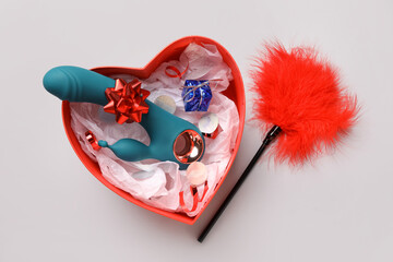 Gift box with vaginal toy and feather stick on grey background