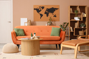 World map on beige wall, sofa, armchair with footrest and table in interior of living room