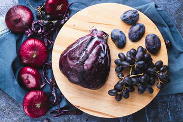 Still life with cut cabbage, red onions, grapes and plums on a wooden board