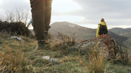 Back view at group of three hiker women going trail forward at scenic landscapes with mountains. Close up legs of tourist in trekking boots walk along rocky path