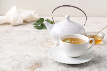 Cup of tasty linden tea with teapot and leaves on white grunge background