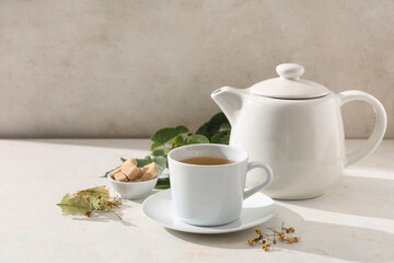 Cup of tasty linden tea with teapot and leaves on white background