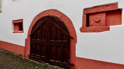 A rustic wooden door is framed by a vibrant peach-colored wall, showcasing unique architectural details around it. The building reflects historical charm and character.
