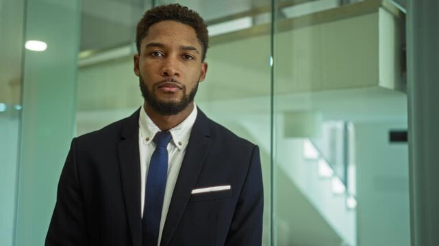 Young businessman standing in a modern office wearing a suit and tie with a glass wall in the background