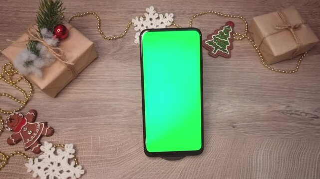 Green screen smartphone lying on wooden table next to beads , snowflakes, a Christmas tree , gifts fnd DIY Christmas decorations. Christmas mockup top view.