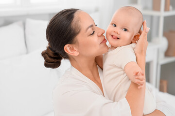 Mother with her little baby showing tongue in bedroom, closeup