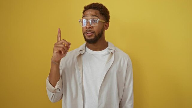 Young man making a gesture of having an idea over an isolated yellow background, showing expressions of thinking and realization while wearing glasses.