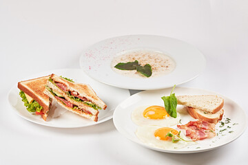 Three plates with cream soup, scrambled eggs and toasts, artistically presented on a black background framed by vegetables and flowers. Culinary art. Food artistry