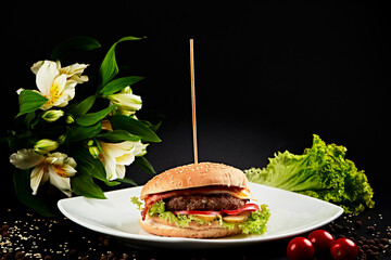 Plate with hamburger, artistically presented on a black background framed by vegetables and...