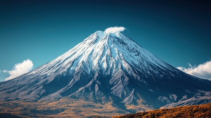 Majestic Mount Fuji with snow-capped peak and autumn foliage at the base, against a clear blue sky.