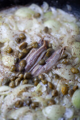 Anchovy, capers are being cooked with onions.