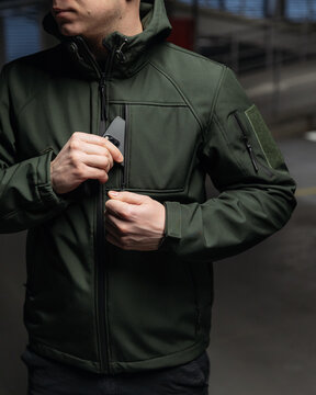 close-up photo of a man taking out a phone from his jacket pocket on a dark background under a lantern