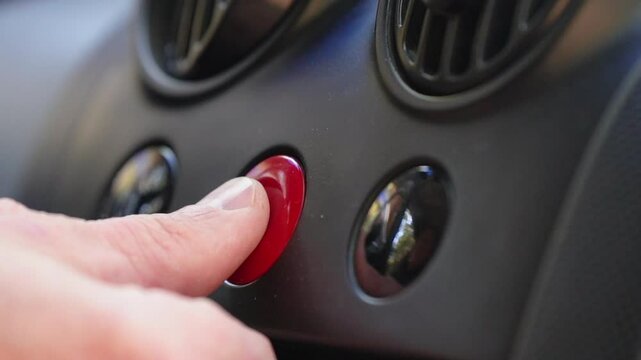 Driver's hand pressing red emergency button on car dashboard to turn on hazard lights. Emergency incident