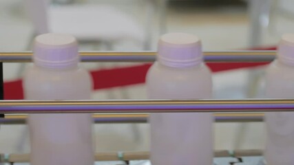 Conveyor belt of bottle shrink sleeve labeling machine with moving empty white plastic bottles at packaging exhibition, factory, plant: close up, side view, demonstration mode, production line