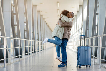 Loving Happy Young african couple embracing joyfully in the airport terminal, romantic man lifting woman off the ground, joyful spouses reunited after long time apart, happy to see each other, copy
