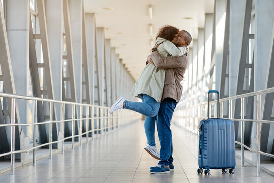 Loving Happy Young african couple embracing joyfully in the airport terminal, romantic man lifting woman off the ground, joyful spouses reunited after long time apart, happy to see each other, copy