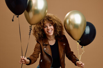 Happy mixed race woman holding black and balloons while looking at camera. © Drazen