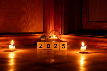 2025 written on cubes and a light bulb at home on the floor with candles in the dark, new year...
