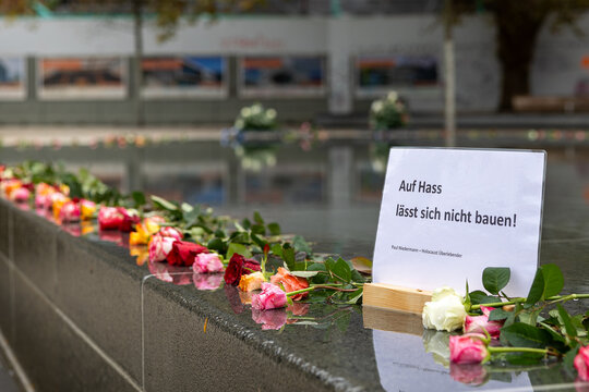 Rosen liegen am Rand eines Gedenkbrunnens, begleitet von einem Schild mit der Aufschrift "Auf Hass l&auml;sst sich nicht bauen" von Paul Niedermann, einem Holocaust-&Uuml;berlebenden.