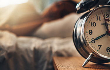 Alarm clock, table and person sleeping, relax and resting in bedroom for energy or lazy at home. Time, bed and oversleeping with fatigue, morning and tired on comfortable mattress for peace or calm