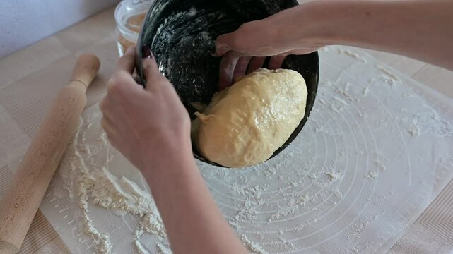 Baking ingredients for baking sweet buns, woman hands spread the dough from a black bowl on a table on a silicone mat